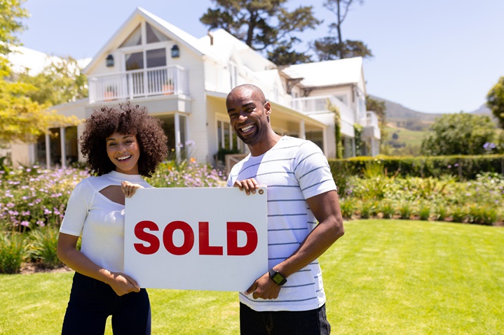 couple holding sold sign in front of house
